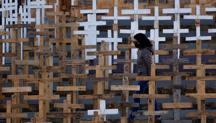 Женщина в маске идет среди сотен крестов